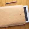 natúr színű bőr IPad vagy tablet tartó rombuszmintás felig kilógó fehér tablettel mellette ceruzával