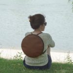 Lulla nevű kollekció kör alakú barna színű bőr desing táska női modell hátán vízparton