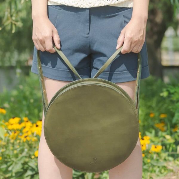 lulla nevű olajzöld kör alakú desing bőr variálható hátizsák vagy válltáska modell kezében előlnézetből.